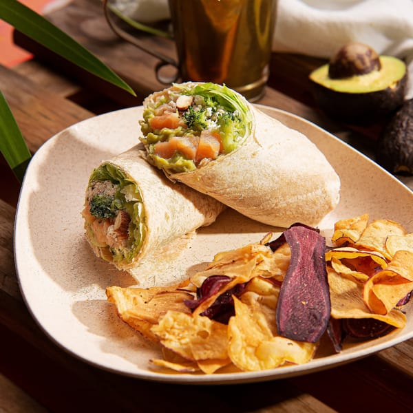 Two wraps filled with salmon, avocado, and broccoli, served with colorful root vegetable chips.